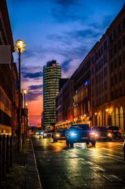 Berlin, Almanya. 14 Eylül 2020. Şehrin şehir merkezindeki caddede gün batımından önce gün batımında uzun pozlama. Eski tuğladan binaları olan modern mimari gökdelen ofisi. Farların aydınlatılması.