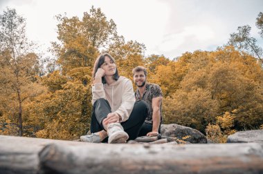 Sıcak tonlarda sonbahar fotosferi, doğal cilt tonları. Güzel bir çift, kanyon deresinin üzerindeki tahta köprüde oturuyor. Aşkta doğada birlikte vakit geçiririz. Balayı seyahati sırasında dinlenme. Mutlu insanlar..