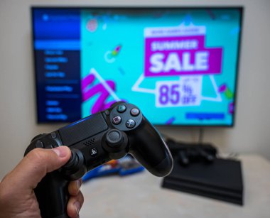 Chengdu, Çin, 12 Ağustos 2019. PS4 oyun mağazasında yaz indirimi. Ön sipariş, indirme, evdeki büyük LCD ekranda Sony Play Station 4 Pro oyunu. Kontrolcü elinde..