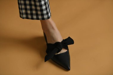 Şık kadın ayakkabısı, keskin çorap, eşsiz küre topuklu ve üstünde bez fiyonk. Güzel ayak bileği ve ekose pantolon askıları. Doğal renkler ve gölgeler, kahverengi arka planda izole edilmiş. Moda konsepti.