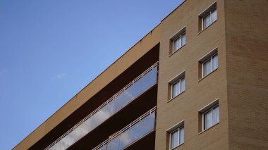 Gökyüzüne karşı tuğla bina cephesi ve cam balkonlar