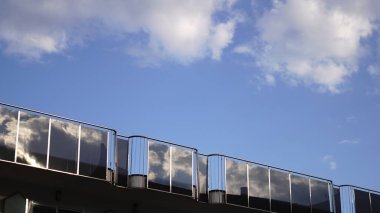 Raylı ayna camları bulutları yansıtıyor.