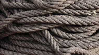 Sıkıca sarılmış, yıpranmış, pürüzlü, lifli dokusu olan gri bir ip.