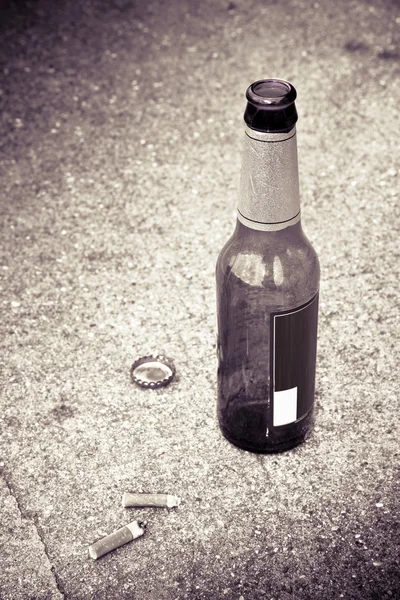 Bottle of beer resting on the ground with three cigarette's butts Stock Photo
