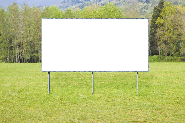 Blank billboard against a green mowed lawn with trees in the countryside - image with copy space