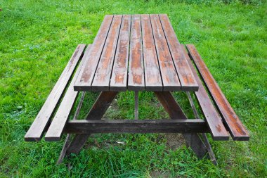 Kamu parkının yeşil çayırında boş ahşap piknik masası..