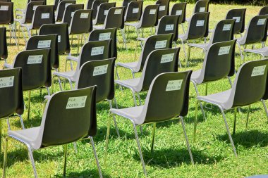 Coronavirus Sars-Cov-2 nedeniyle aralıklı siyah plastik koltuklu açık hava sineması - Koltukların arkasında koltuk numarası ve saygı duyulacak satır - FILA ham anlamına gelir - POSTO PLACE