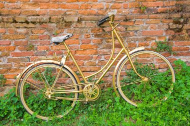 GOLDEN VINTAGE BICYCLE AGAINST RUSTIC BRICK WALL SYMBOL OF FREEDOM AND NOSTALGIA - Conceptual image of sustainability, retro lifestyle, urban travel, creativity and unique design