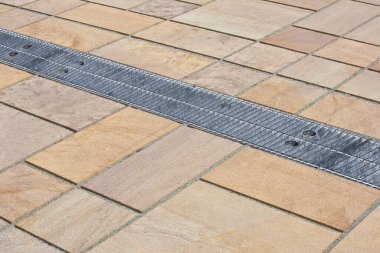 METAL RAINWATER COLLECTION GRID IN A PEDESTRIAN ZONE with concrete flooring made with blocks of rectangular shape