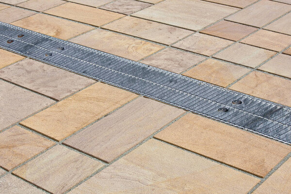 METAL RAINWATER COLLECTION GRID IN A PEDESTRIAN ZONE with concrete flooring made with blocks of rectangular shape