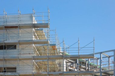 INCOMPLETE MODERN CONSTRUCTION SITE WITH METAL SCAFFOLDING AND URBAN DEVELOPMENT - Concept of architecture, progress, industry, engineering, business growth and modernization - Image with copy space