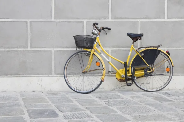 Oude geel fiets op een stenen bestrating tegen een muur gips — Stockfoto