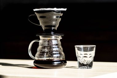 Bir hunide kahve yapmak. Hario V60 kahve hunisi sunucuda. Koyu arkaplanı olan güzel bir masa. Kahve spesiyalitesini demleme süreci. buhar kahveden geliyor.