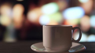 Gece şehrine bakan pencerenin önündeki bir kafede, ahşap masanın üzerinde bir fincan kahve.