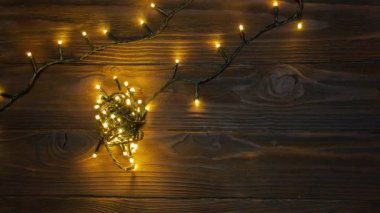 Hareket animasyonunu durdur. Sarı Noel ışıkları zinciri ahşap yüzeyde gevşiyor ve yanıp sönüyor.