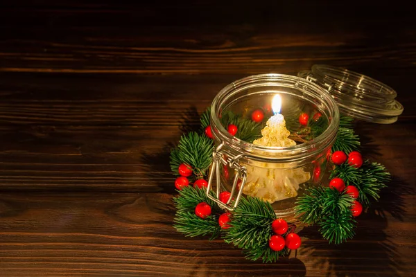 Candle is burning inside glass jar with christmas wreath.