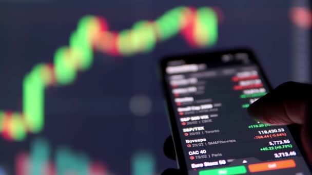 スマートフォンやパソコンの画面で金融市場の情報を見る男 — ストック動画