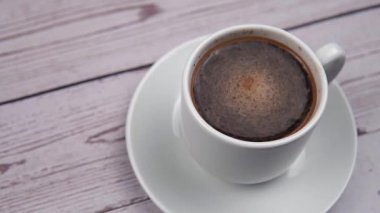 Beyaz fincanda köpük ve ahşap arka planda kahve.