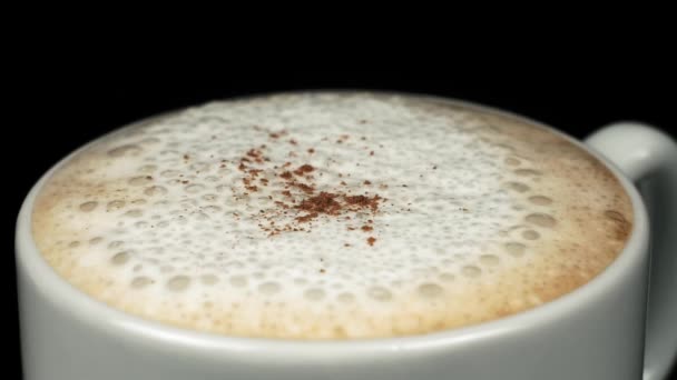 Kávéhab Szórása Fahéjporral Egy Csészében Fekete Alapon Közelkép Lassú Mozgás — Stock videók