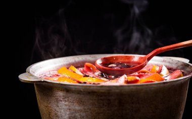 Büyük çaydanlık dolusu geleneksel sıcak buharlı Noel içeceği kaynatılmış kırmızı baharatlı şarap elma ve siyah arka planda tahta kaşıkla narenciye. Noel partisi.