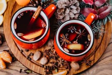 İki kırmızı Noel bardağı baharatlı kırmızı şarap, tarçın çubuğu, elma ve narenciye portakalı, limon renginde ahşap masa, üst manzara. Bir kupa sıcak şarap, geleneksel noel içeceği..