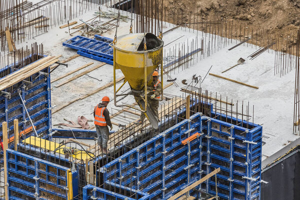 Concreting work at the construction site. ?onstruction workers pour liquid concrete from cement concrete hopper to fromwork installation.