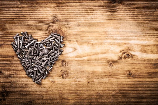 A heart shaped figure laid out from screws on vintage brown wooden board. Concept of metallic artificial heart machine, robot, mechanism, Valentine Day, strong eternal love. Free text space.