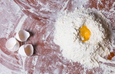 Makarna için hamur yoğurmak ya da üstünde çiğ yumurta olan pizza için buğday beyazı un yığınıyla fırınlama manzarası. Kapatın. Ev yapımı pişirme konsepti.