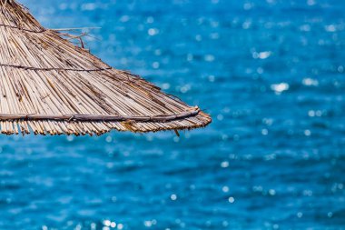 Mavi turkuaz bir arka planda sazlık plaj şemsiyelerine yakın çekim. Tropik tatil köyü yaz arkaplanı. İnsan yok. Boş metin alanı.