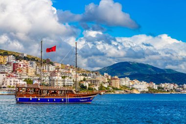 Arnavutluk 'un Saranda kenti - Eylül 2019: Saranda kentinin arka planında Arnavutluk' un Saranda kentinde deniz turları için Onhesmus adlı eski gemi yelkenli direği bulunuyor. Bulutlu bir gün. Deniz manzarası.