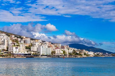 Arnavutluk 'un Saranda Körfezi ve kasabasının panoramik manzarası ve kıyı boyunca oteller. Güneşli bir yaz günü. Gökyüzünde güzel bulutlar. Ufukta görünen Arnavut dağları. Sakin mavi deniz.