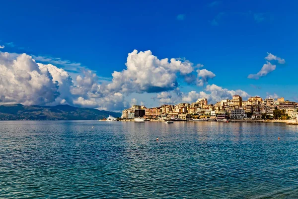 Arnavutluk 'un sahil şeridi boyunca yer alan Saranda Körfezi, kasaba ve şehir limanının panoramik manzarası. Güneşli bir yaz günü. Gökyüzünde güzel bulutlar. Korfu adası ufukta görünüyor. Sakin mavi deniz.
