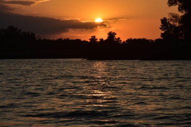 Nehirde güzel bir gün batımı. Önünde bulutlar ve ağaçlar var.