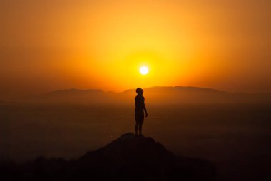 Dağda güneşin altında duran bir adamın silueti.