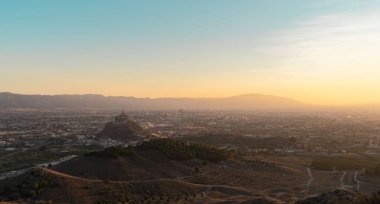 Ufukta dağlar olan bir şehrin panoramik manzarası. Bazı küçük tepeler ve dağda bir İsa heykeli görüyoruz. Adı Cristo de Montagudo. Murcia, İspanya 'da bulunuyor.