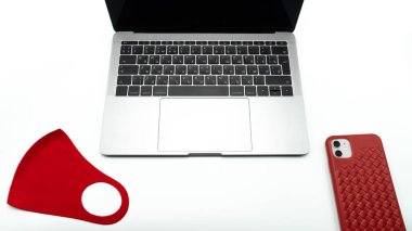 Kırmızı koruyucu maske ve telefon kırmızı bir çantada dizüstü bilgisayarın yanında, görüntüyü kapat. Ağ iletişimi, online alışveriş ya da laboratuvar işi kavramı. COVID-19. Kişisel izolasyon ve sosyal uzaklık
