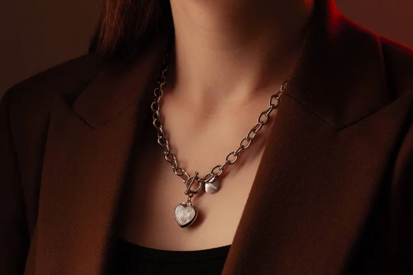 Portrait en gros plan de jeune femme à la peau soyeuse parfaite, démontrant une chaîne de bijoux en argent avec médaillon sur le cou dans une veste marron — Photo