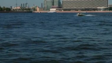 St. Petersburg, Rusya - Haziran 2021. Neva Nehri boyunca hızlı bir tekne hareket eder. Nehirde büyük dalgalar var. Arka planda iş merkezlerini, Aurora kruvazörünü ve turistik yerleri görebilirsiniz. 4K