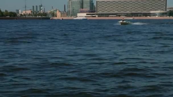 Sint-Petersburg, Rusland - juni 2021. Een snelle boot vaart langs de Neva rivier. Grote golven op de rivier. Op de achtergrond ziet u zakelijke centra, de cruiser Aurora en toeristische attracties. 4K — Stockvideo