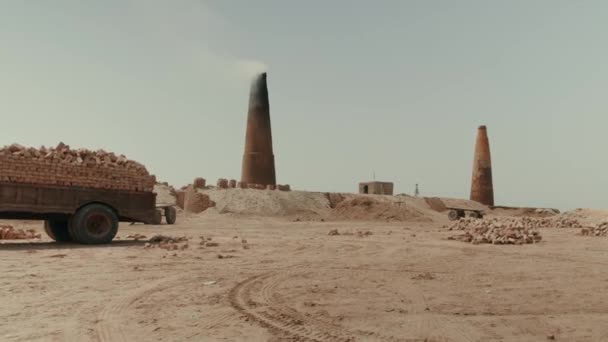 Una fábrica de ladrillos en Pakistán que utiliza mano de obra esclava. En la arena hay un remolque con ladrillos ya hechos. Sobre el fondo de la tubería de la que hay humo — Vídeos de Stock