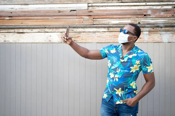 Covid-19 salgınında maskeli genç bir zenci korunmak için. Afro-Amerikalı bir adam cep telefonlu Afro-Amerikan bir fotoğraf çekiyor..