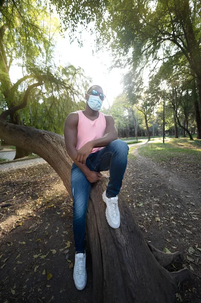 A young black man with a mask in the covid-19 pandemic season for protection. Portrait of a young african man with a face mask in park.