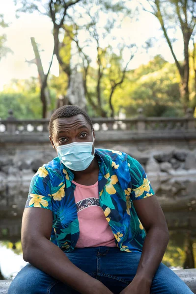A young black man with a mask in the covid-19 pandemic season for protection. Portrait of a young african man with a face mask in park. Outdoors portrait