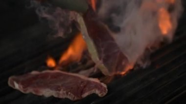 Şef ızgarada et çeviriyor. Ateş ağır çekimde yanıyor. Izgarada sulu biftek. BBQ Video Konsepti 