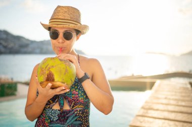 Mutlu kadın havuzda dinleniyor ve hindistan cevizi suyu içiyor. Açık havuzda gülümseyen sevimli bir kadının portresi. Tropik bir havuzda gezgin kavramı. Açık hava yaşam tarzı.