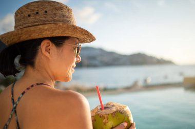 Mutlu kadın havuzda dinleniyor ve hindistan cevizi suyu içiyor. Açık havuzda gülümseyen sevimli bir kadının portresi. Tropik bir havuzda gezgin kavramı. Açık hava yaşam tarzı.