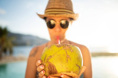 Mutlu kadın havuzda dinleniyor ve hindistan cevizi suyu içiyor. Açık havuzda gülümseyen sevimli bir kadının portresi. Tropik bir havuzda gezgin kavramı. Açık hava yaşam tarzı.