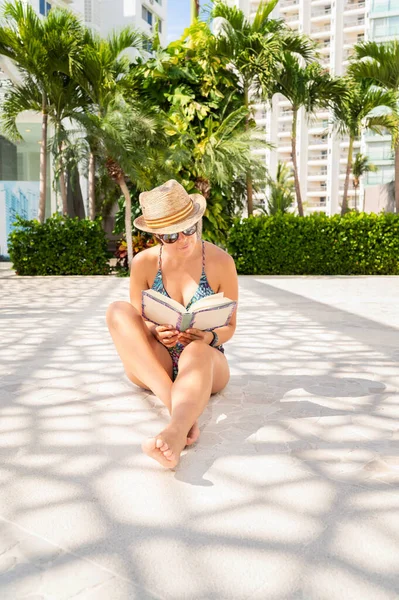 戴着夏帽的女人穿着漂亮的泳衣 戴着漂亮的太阳镜 在游泳池边看书 放松和旅行概念 — 图库照片