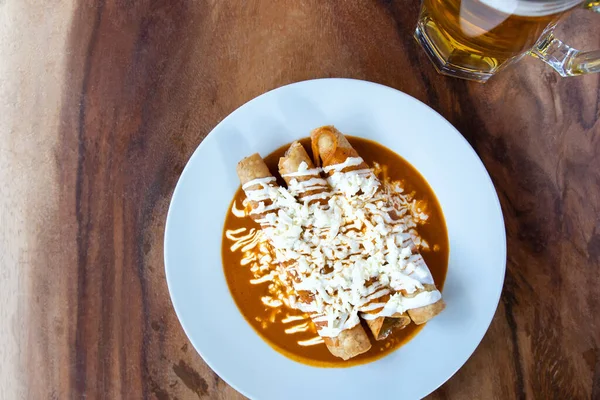 Boğulmuş Meksika flütleri, kırmızı soslu geleneksel Meksika yemekleri. Boğulmuş taco. Geleneksel Meksika yemekleri. Tahta arka planda Meksika yemeği. Geleneksel Meksika yemeği konsepti.