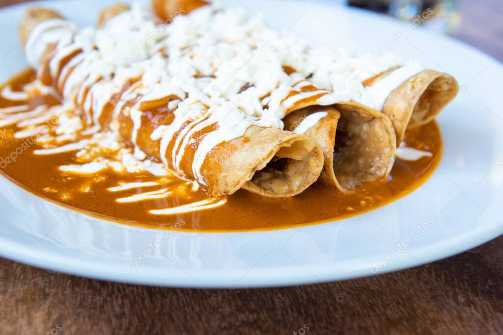Flautas mexicanas ahogadas, comida tradicional mexicana con salsa roja
